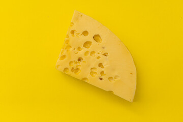 A piece of cheese with holes lies on a yellow background, monochrome products