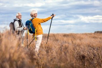 Active senior couple with backpacks hiking together in nature on autumn day.