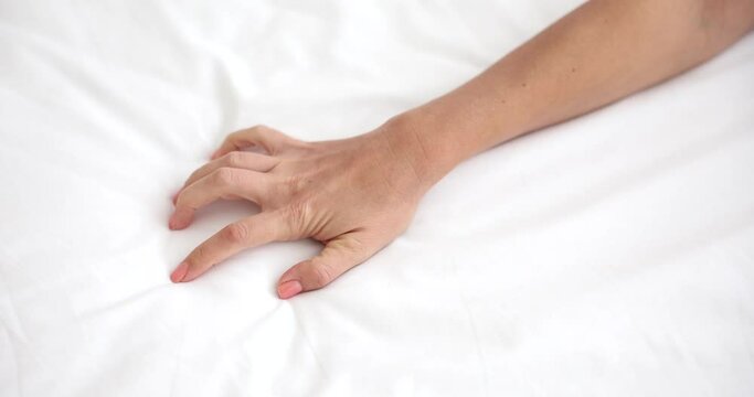 Woman hand passionately clutches sheet on bed