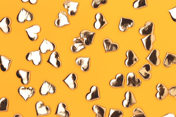 Texture made of gold colored hearts confetti on a yellow background.