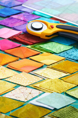 Pile of colorful fabric diamonds on cutter mat, quilting accessories