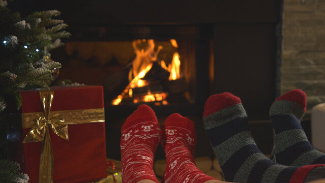CLOSE UP: Couple rest by fireplace and warming up their feet in Christmas socks