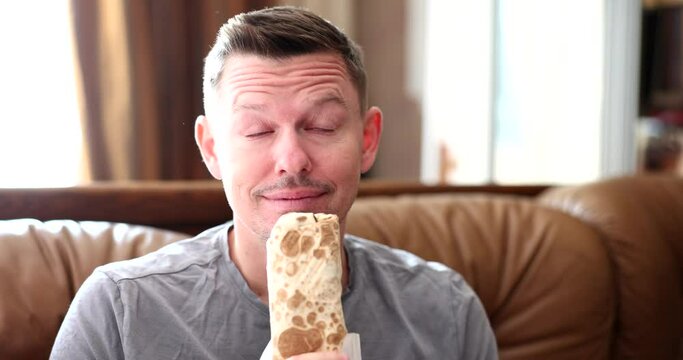 Happy man eating delicious shawarma at home