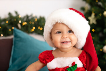 Merry Christmas. Portrait of a cute little one-year-old girl baby in a cozy bedroom dressed up for the holiday. Lifestyle