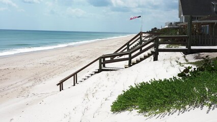 White sand beach in Florida. In the distance, the waves of the ocean, a wooden staircase to the beach and a weather vane with the symbols of the American flag waving in the wind - Powered by Adobe