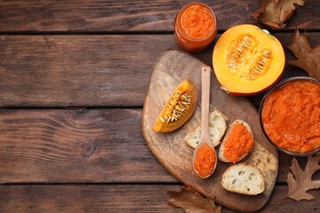 Slices of bread with delicious pumpkin jam and fresh pumpkin on wooden table, flat lay. Space for text