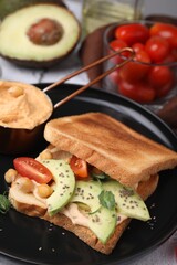 Delicious sandwich with hummus and vegetables on white textured table, closeup