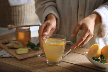 Woman making aromatic ginger tea at wooden table indoors, closeup