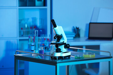 Modern microscope and glassware with colorful liquids on metal table in laboratory, toned in blue