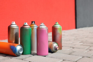 Cans of different spray paints on pavement near wall, space for text