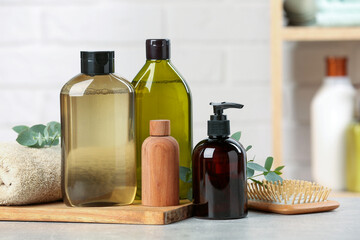 Shampoo bottles, hair brush, towel and leaves on light grey table