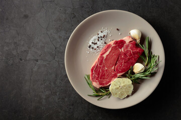Raw beef meat steak with rosemary, garlic, salt, and pepper.