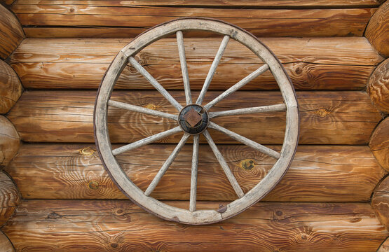 A section of a log wall with an old wagon wheel attached to it. © miraleks