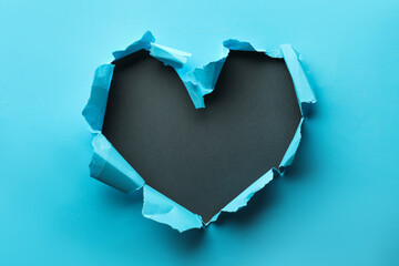 Naklejka na ściany i meble Torn heart shaped hole in light blue paper on black background