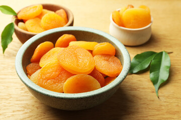 Tasty apricots with green leaves on wooden table, closeup. Dried fruits
