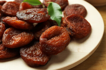 Plate of tasty apricots and green leaves on wooden table, closeup. Dried fruits