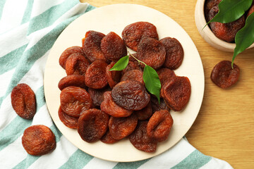 Tasty apricots and green leaves with plate on wooden table, flat lay. Dried fruits
