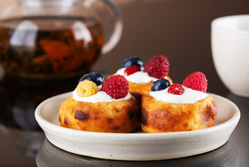 Russian dessert cheese pancakes with blueberries, raspberries and sour cream with cup of tea.