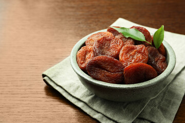 Bowl of tasty apricots with leaves on wooden table, space for text. Dried fruits