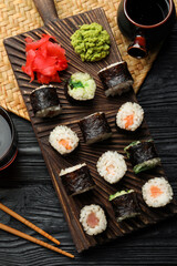 Tasty sushi rolls served on black wooden table, flat lay