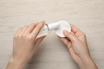 Woman pouring micellar water from bottle onto cotton pad at wooden table, top view © New Africa