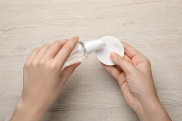 Woman pouring micellar water from bottle onto cotton pad at wooden table, top view