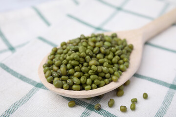 Wooden spoon with mung beans on kitchen towel, closeup