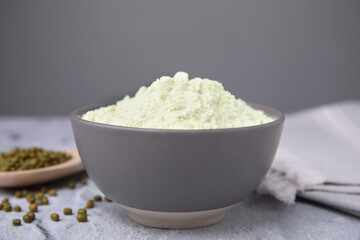 Mung bean flour in bowl and seeds on white textured table