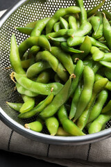 Sieve with green edamame beans in pods on table, closeup
