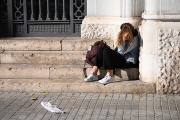 A young, brunette woman sits on a stairs of an historical building in Valencia-Spain while she plays with her long hair.