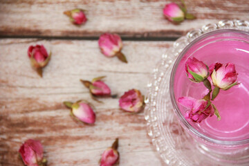 pink tea in a transparent glass mug with small dry buds of natural roses on a wooden background