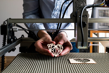 Laser engraving and cutting, woman holding an example of a cut out wooden heart
