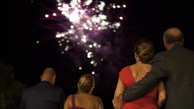 Hand-held shot of well-dressed couples embracing each other while watching a firework display