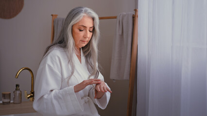 Beautiful grandma 60s lady old senior gray haired female Caucasian woman in bedroom rubbing...