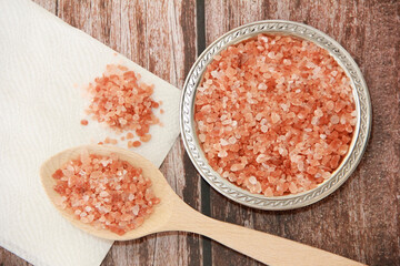 small granules of natural Himalayan salt in a wooden spoon and a decorative metal plate on a wooden background