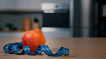 Red apple and tape measure on kitchen table in foreground blurred African man on background guy opening refrigerator fridge searching food to eating dieting lunch cooking dinner meal sport nutrition 