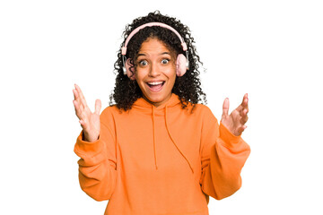 Young Brazilian woman listening to music with headphones isolated receiving a pleasant surprise,...