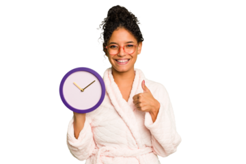 Young brazilian woman wearing a pajama holding a clock isolated smiling and raising thumb up