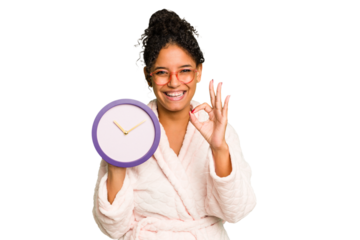Young brazilian woman wearing a pajama holding a clock isolated cheerful and confident showing ok gesture.