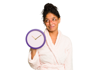 Young brazilian woman wearing a pajama holding a clock isolated dreaming of achieving goals and purposes