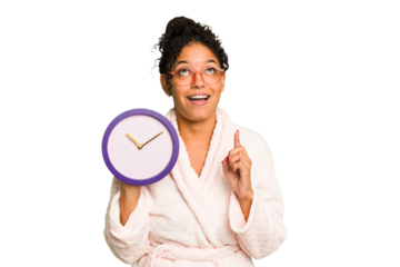 Young brazilian woman wearing a pajama holding a clock isolated pointing upside with opened mouth.