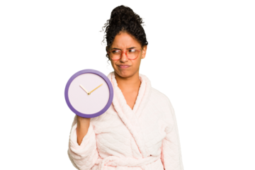 Young brazilian woman wearing a pajama holding a clock isolated confused, feels doubtful and unsure.