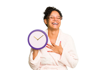 Young brazilian woman wearing a pajama holding a clock isolated laughs out loudly keeping hand on...