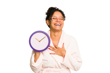 Young brazilian woman wearing a pajama holding a clock isolated laughs out loudly keeping hand on chest.