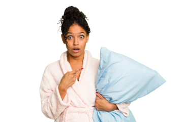 Young brazilian woman wearing a pajama holding a pillow isolated pointing to the side