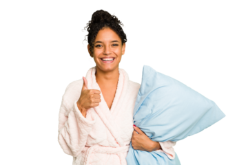 Young brazilian woman wearing a pajama holding a pillow isolated smiling and raising thumb up