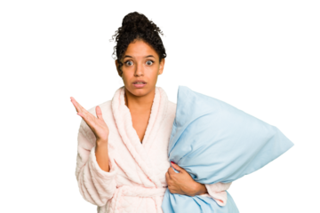 Young brazilian woman wearing a pajama holding a pillow isolated surprised and shocked.
