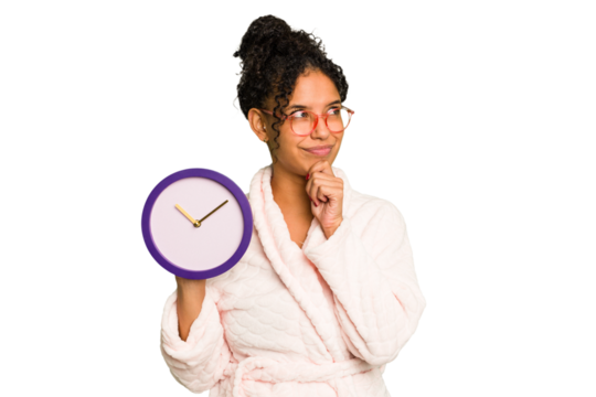 Young brazilian woman wearing a pajama holding a clock isolated looking sideways with doubtful and skeptical expression.