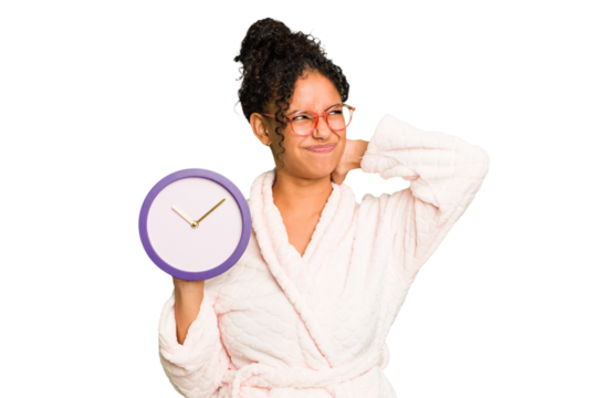 Young brazilian woman wearing a pajama holding a clock isolated touching back of head, thinking and making a choice.