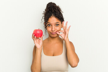 Young brazilian woman holding a red apple isolated with fingers on lips keeping a secret.
